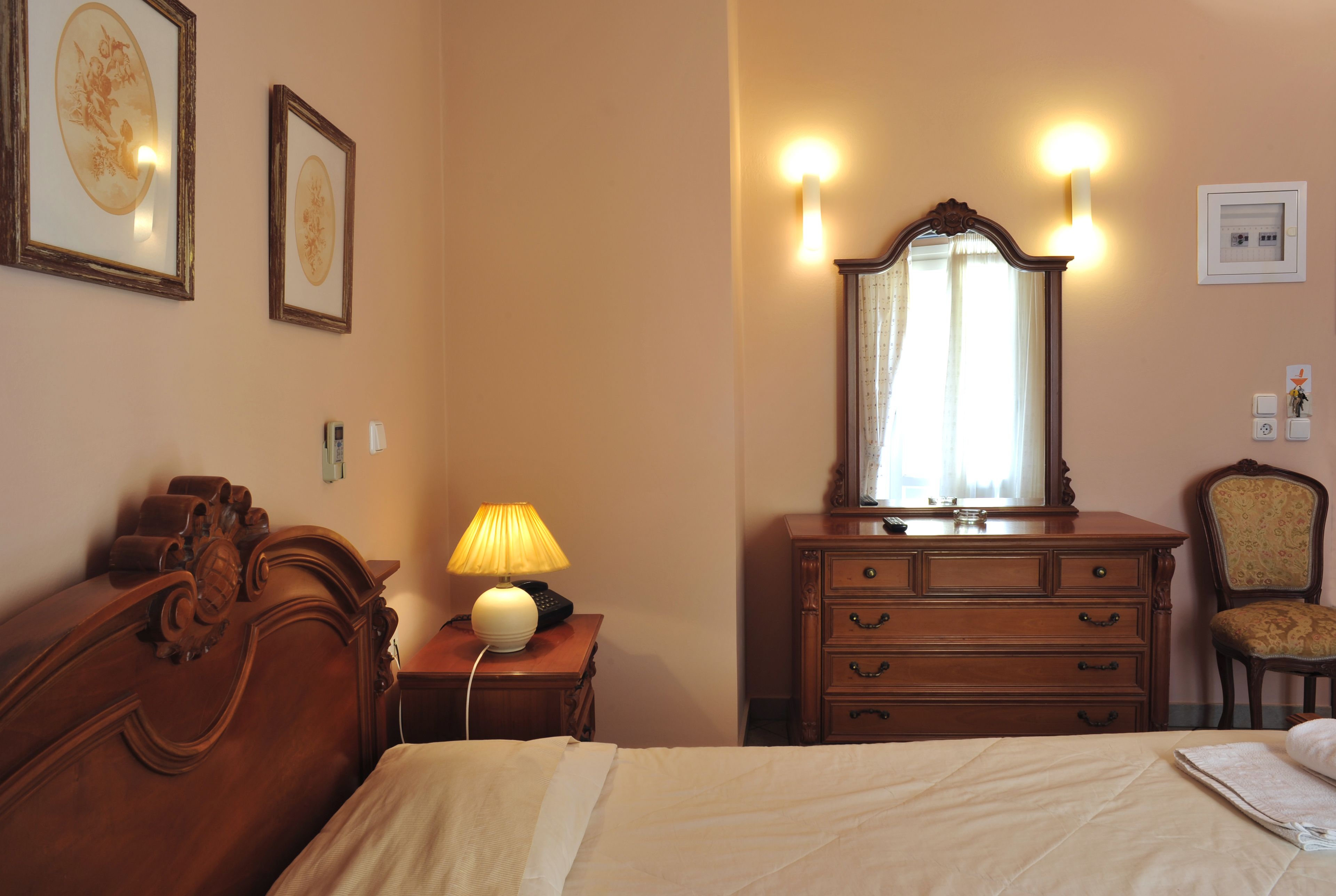 Una habitación de hotel con una cama, un aparador de madera con cajones, un espejo y luces fijadas a la pared.