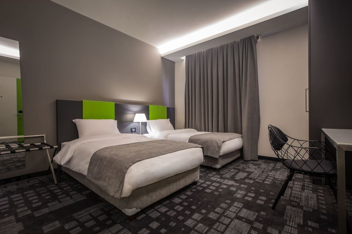 A hotel room with two beds, a desk, a chair, and a large window with curtains.