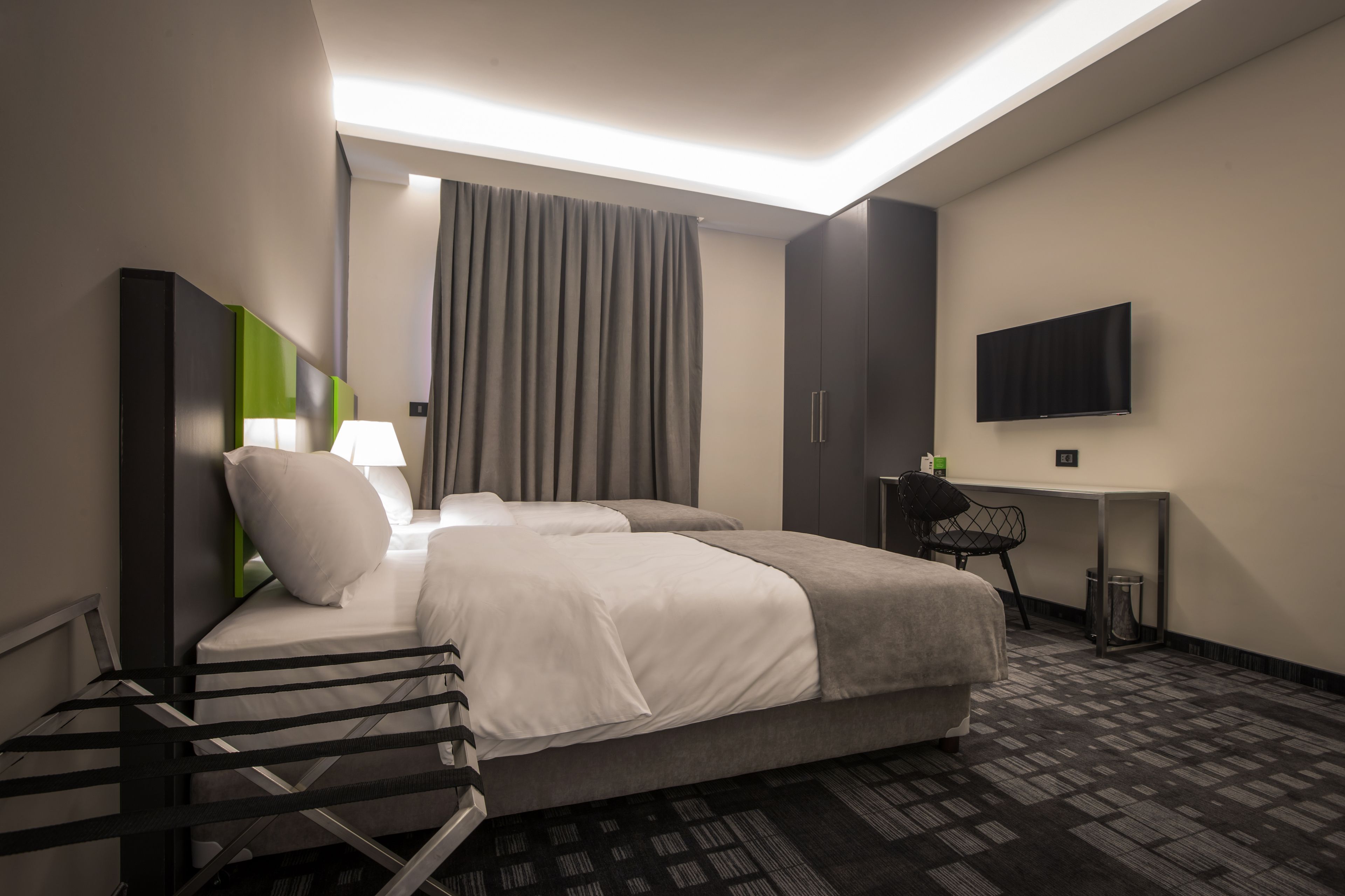 Ein Hotelzimmer mit Bett, Schreibtisch, Stuhl, Fernseher und einem Fenster mit Vorhängen.