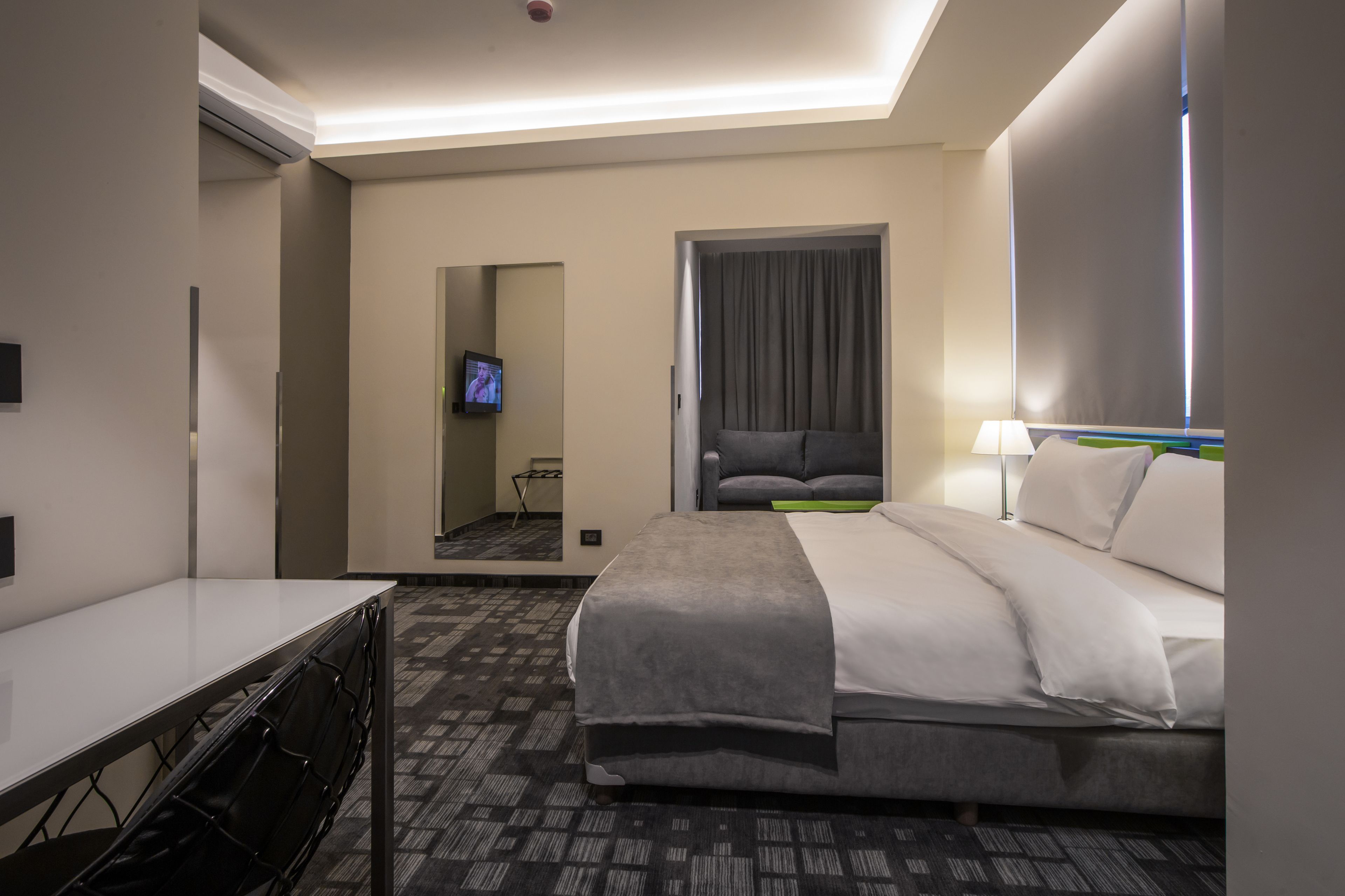 Une chambre d’hôtel avec un lit, un bureau, une chaise, une télévision et une fenêtre avec des rideaux.