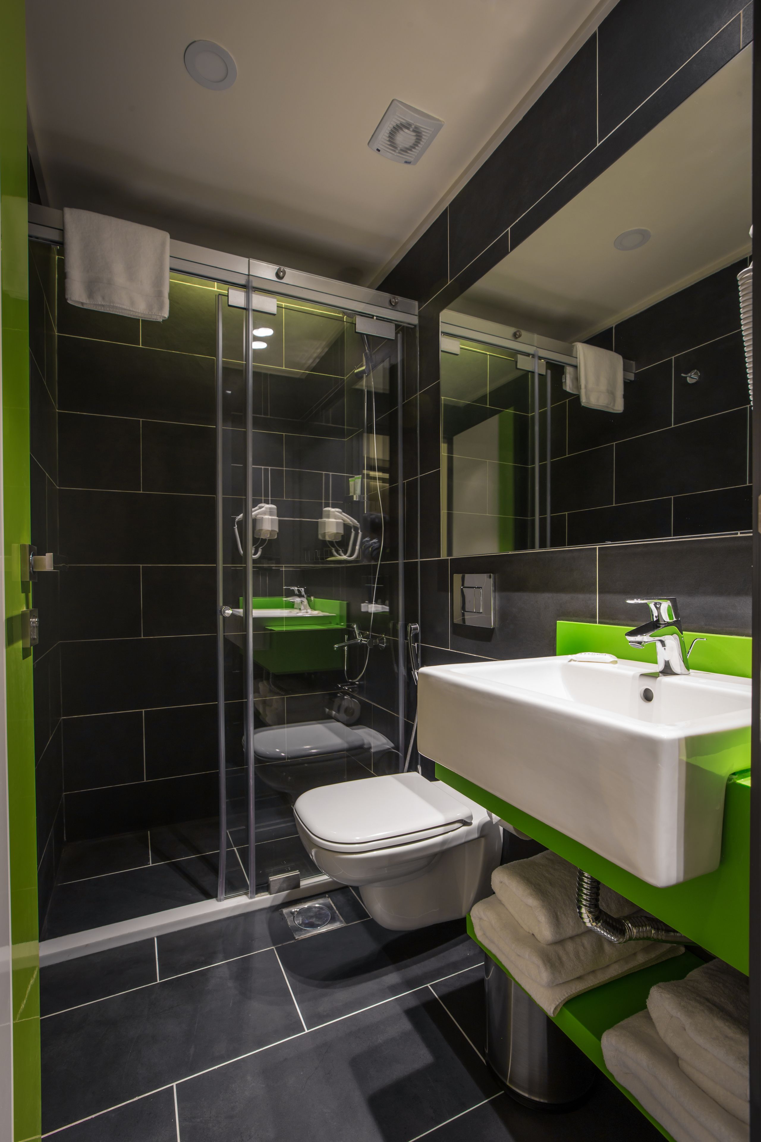 A modern bathroom with a glass shower enclosure, a white sink, and a green vanity.