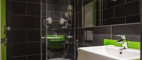 Un baño moderno con cabina de ducha de vidrio, un lavabo blanco y un mueble de tocador verde.