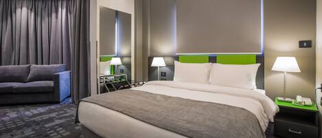 Une chambre d’hôtel avec un grand lit, un canapé, un bureau avec une lampe et un téléphone sur la table de chevet.