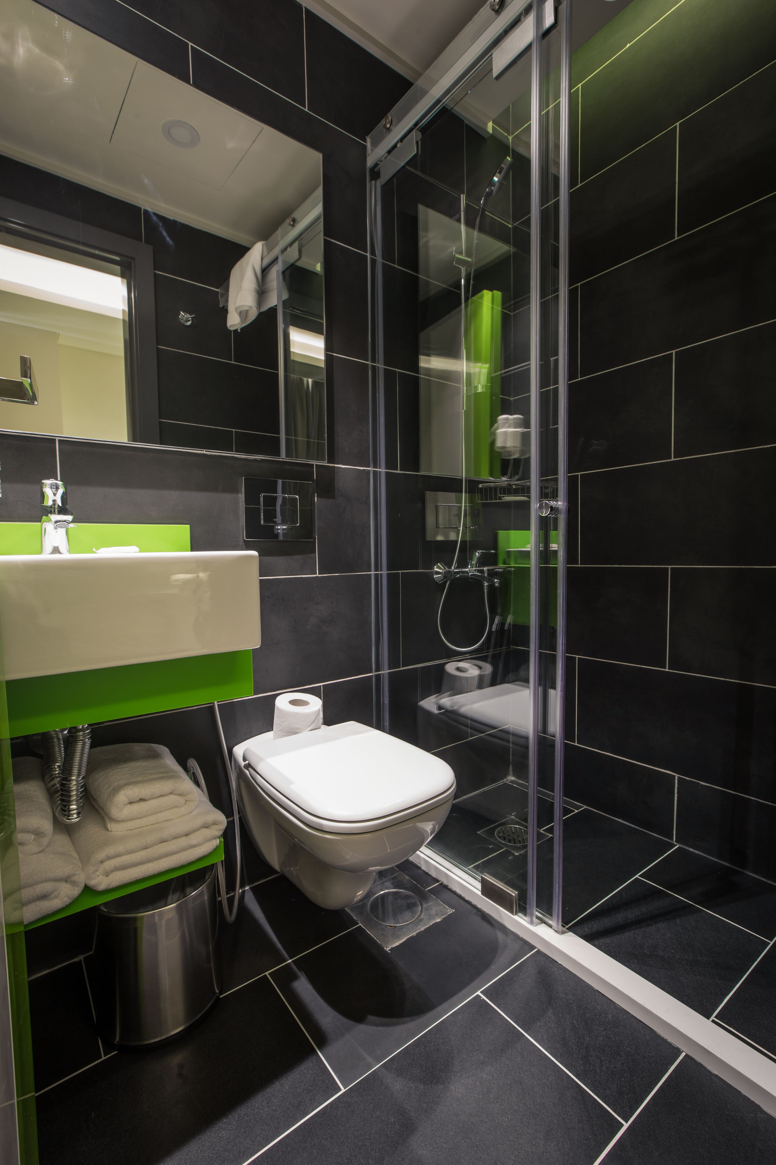 Et moderne badeværelse med en brusekabine i glas, et hvidt toilet og et vaskebord med grønne fliser.