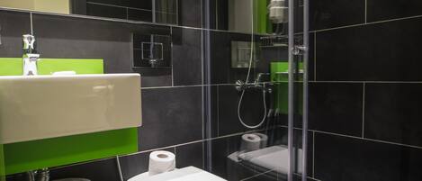 Un baño moderno con ducha acristalada, inodoro blanco y zona de lavabo con azulejos verdes.