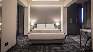 A modern hotel room with a large bed, two bedside tables with lamps, a desk, and a wardrobe.