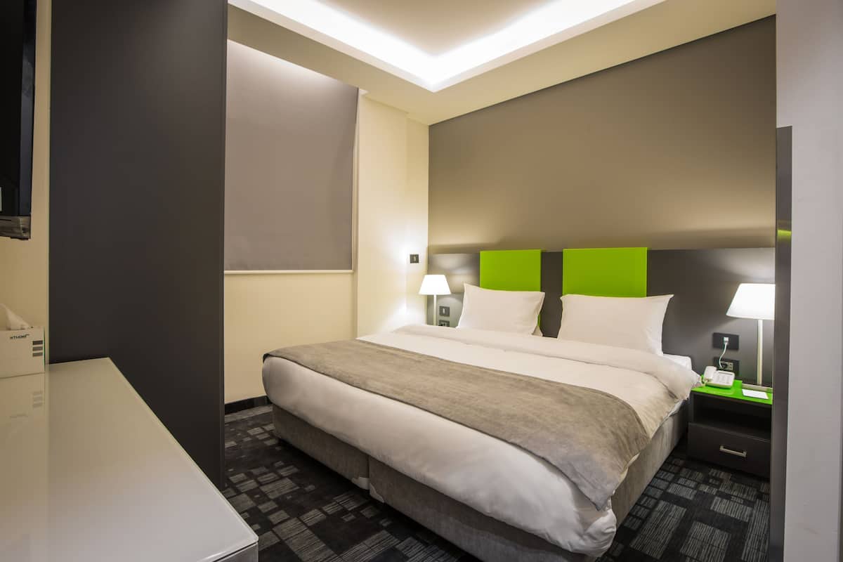 A hotel room with a large bed, bedside tables with lamps, a desk, and a flat-screen TV.