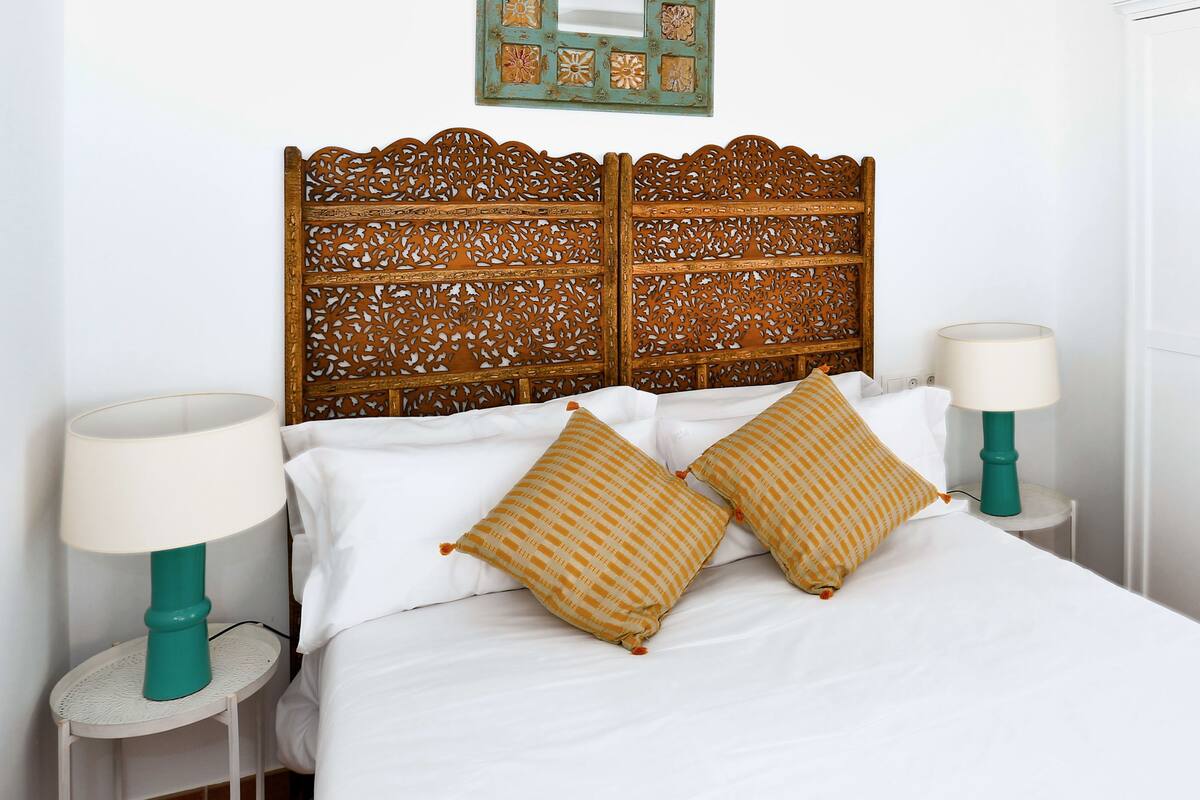 Een bed met een houten hoofdbord, wit beddengoed en twee bedlampjes.