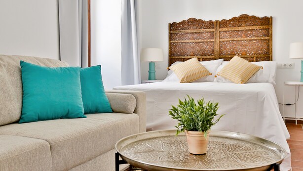 Une chambre à coucher avec un lit, un canapé, une table de chevet et une plante en pot.