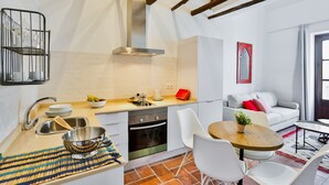 Une cuisine compacte dotée d’appareils électroménagers modernes, un coin repas avec des chaises blanches et un espace salon confortable avec un canapé et une petite table.