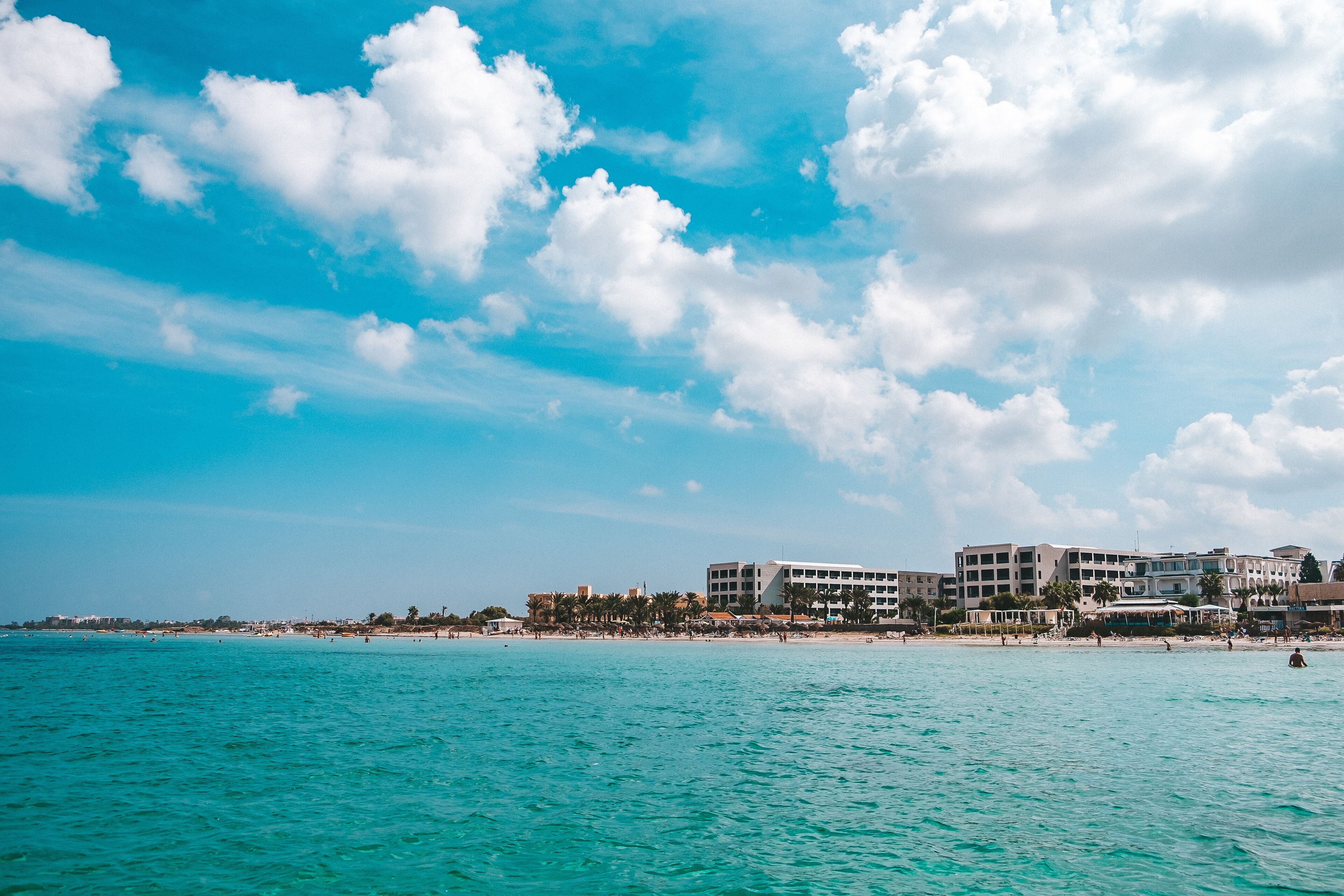 Un hôtel situé sur la côte, avec plusieurs étages, une plage en arrière-plan et un ciel dégagé.