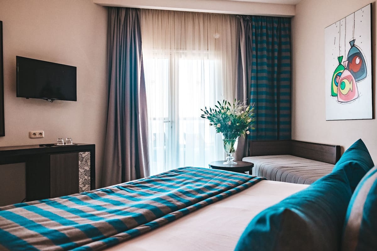 A hotel room with a bed, a TV, a desk, and a window with curtains.