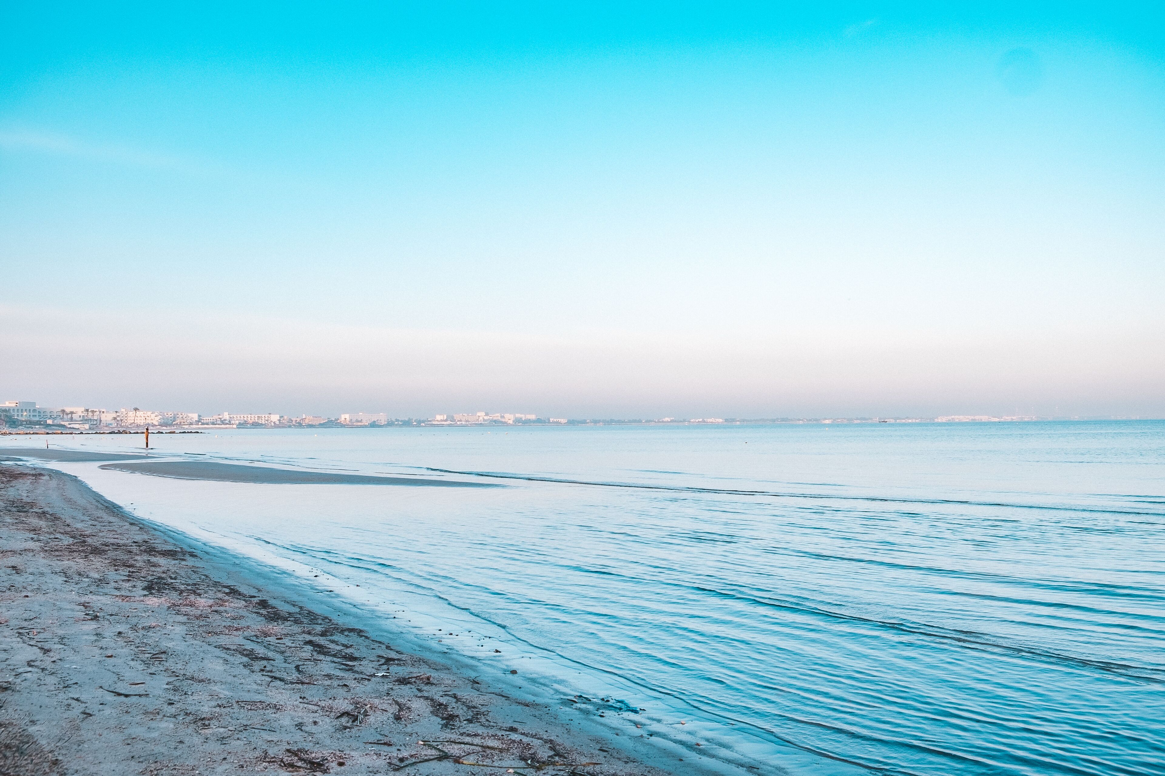 Una playa con vista despejada al mar y el horizonte de una ciudad a lo lejos.