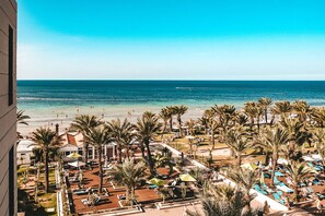 A resort with a beach view, palm trees, and sun loungers.