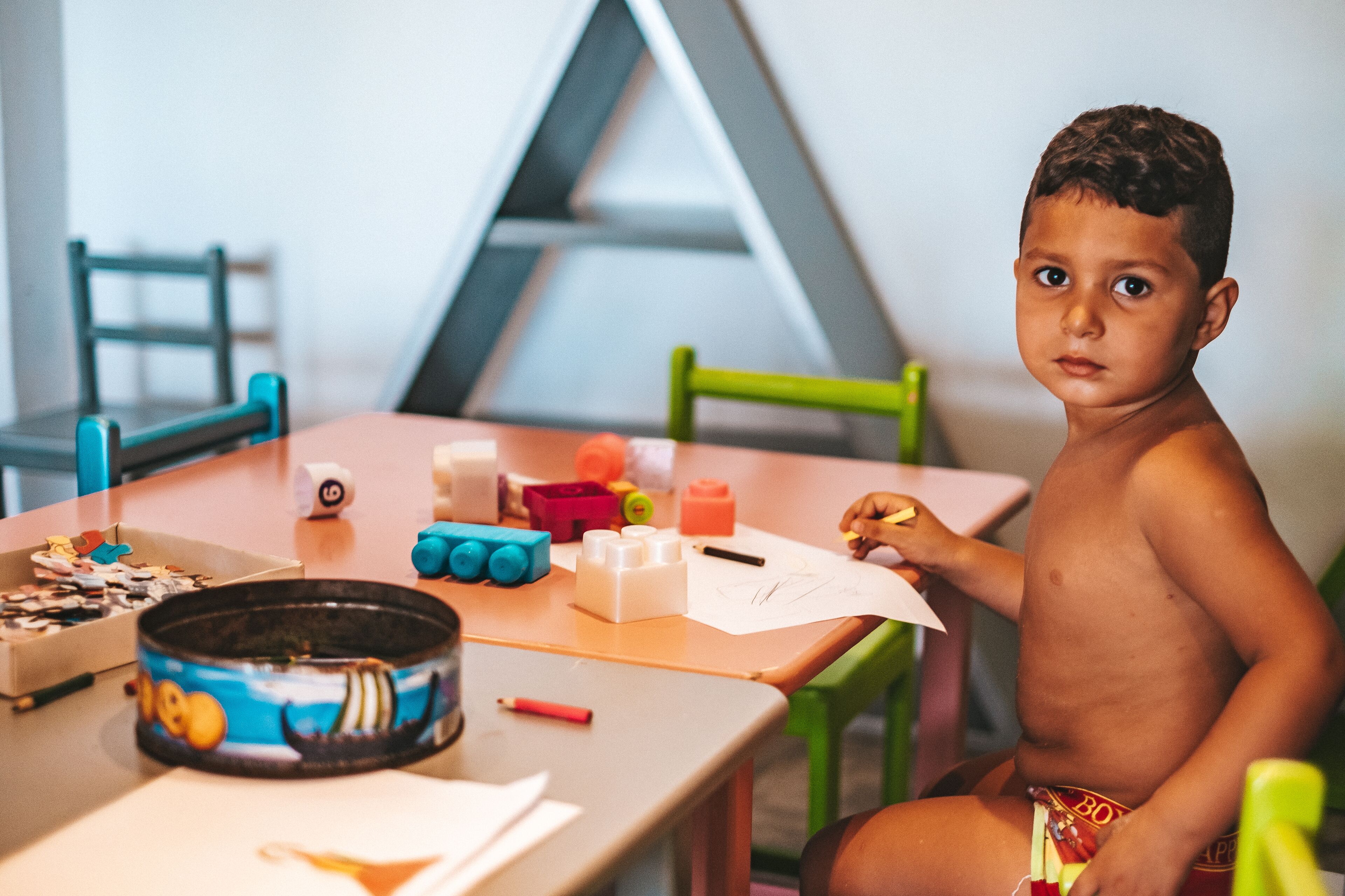 Un niño sentado a una mesa con diversos juguetes y material para dibujar.