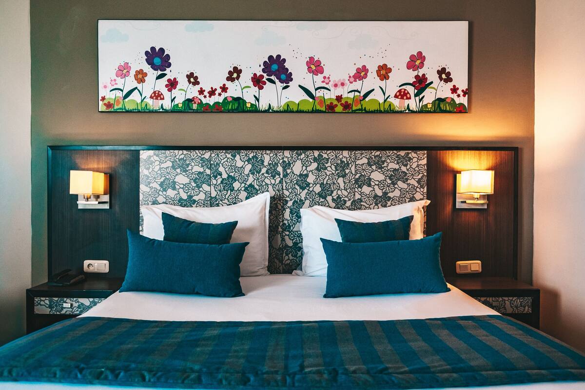 A neatly made bed with blue bedding, two bedside tables with lamps, and a floral artwork above the bed.