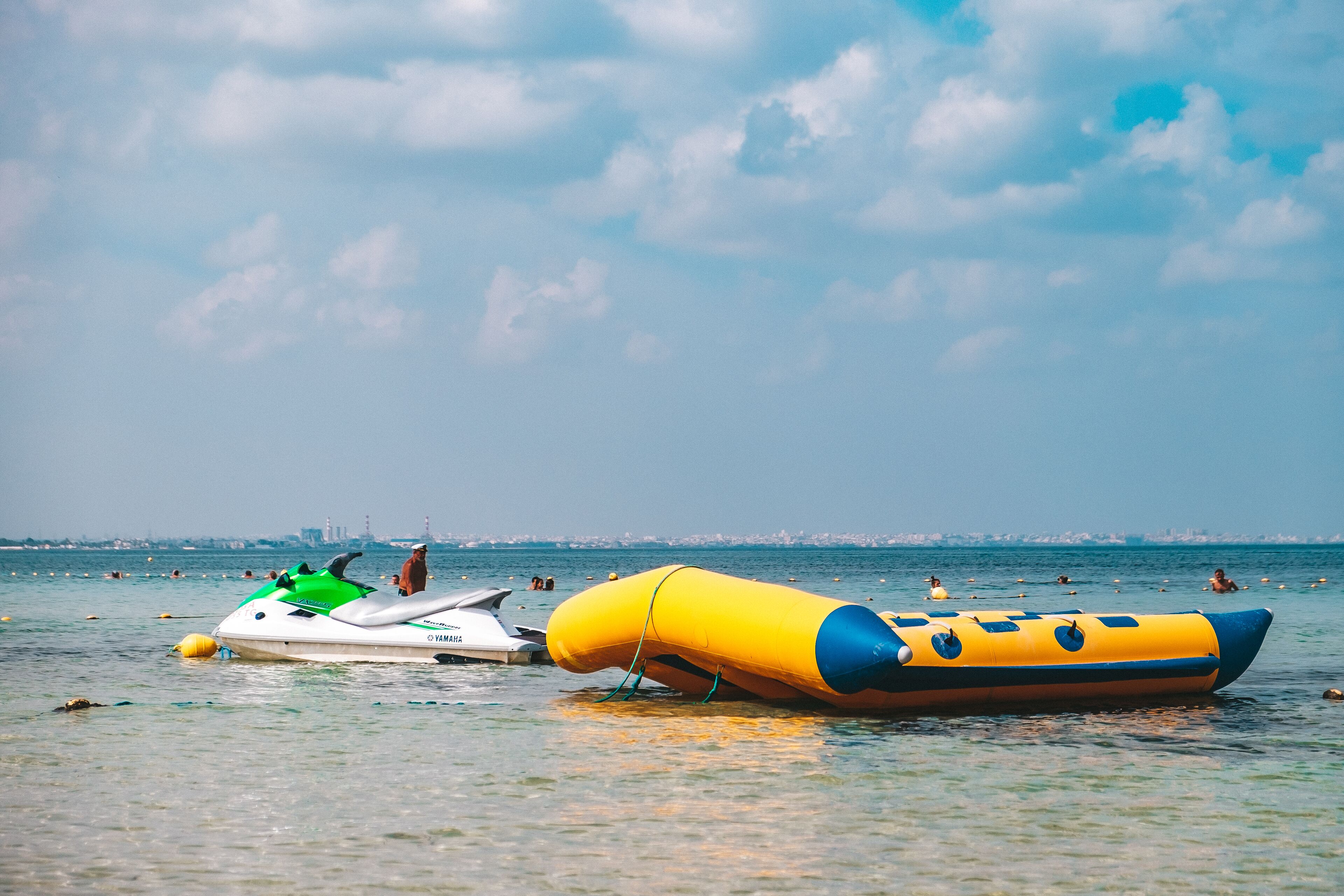 Un jet ski y un bote inflable en un mar tranquilo con un horizonte urbano lejano.