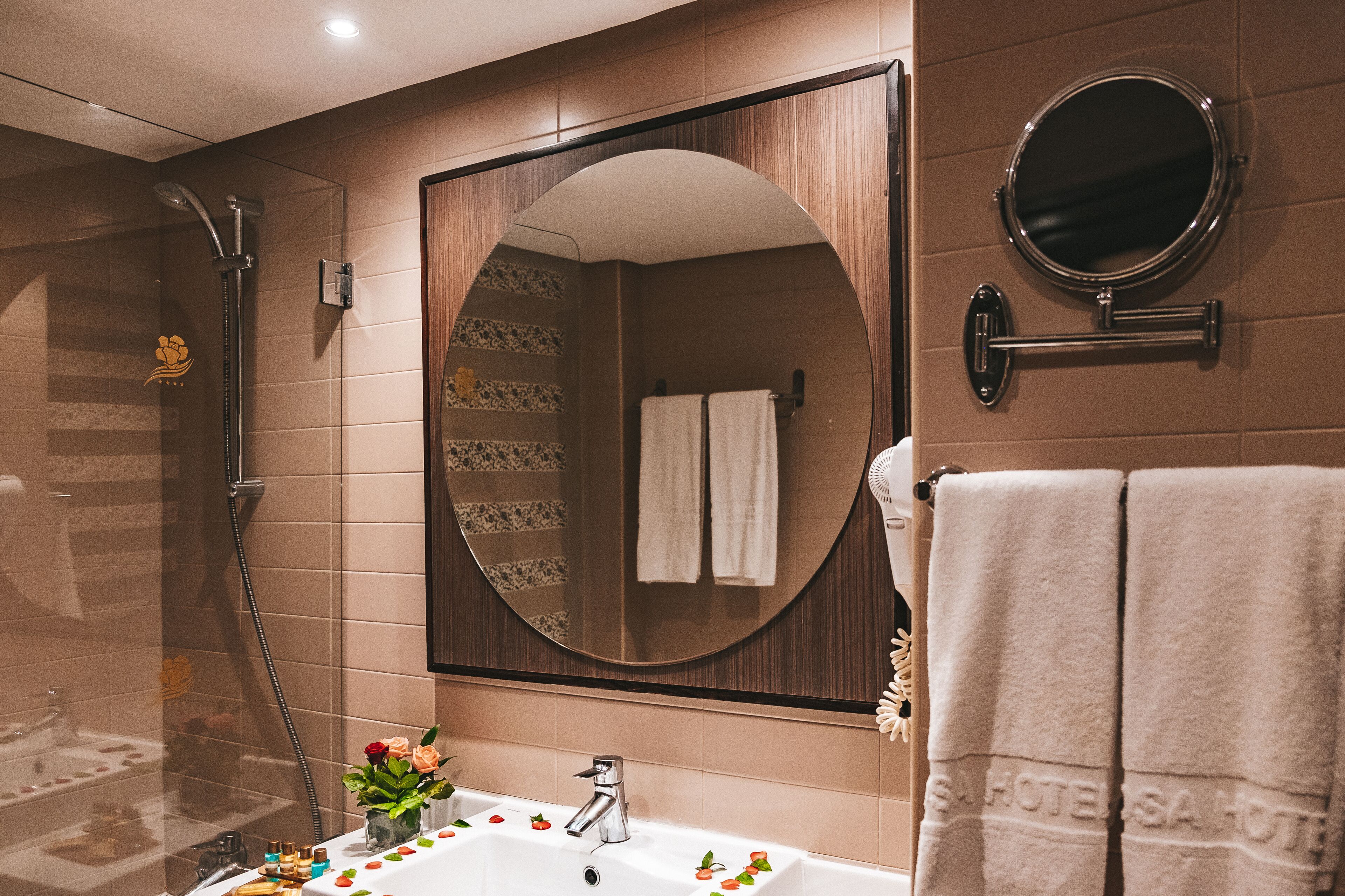 A modern bathroom with a large mirror, a shower, and a sink with decorative flowers.