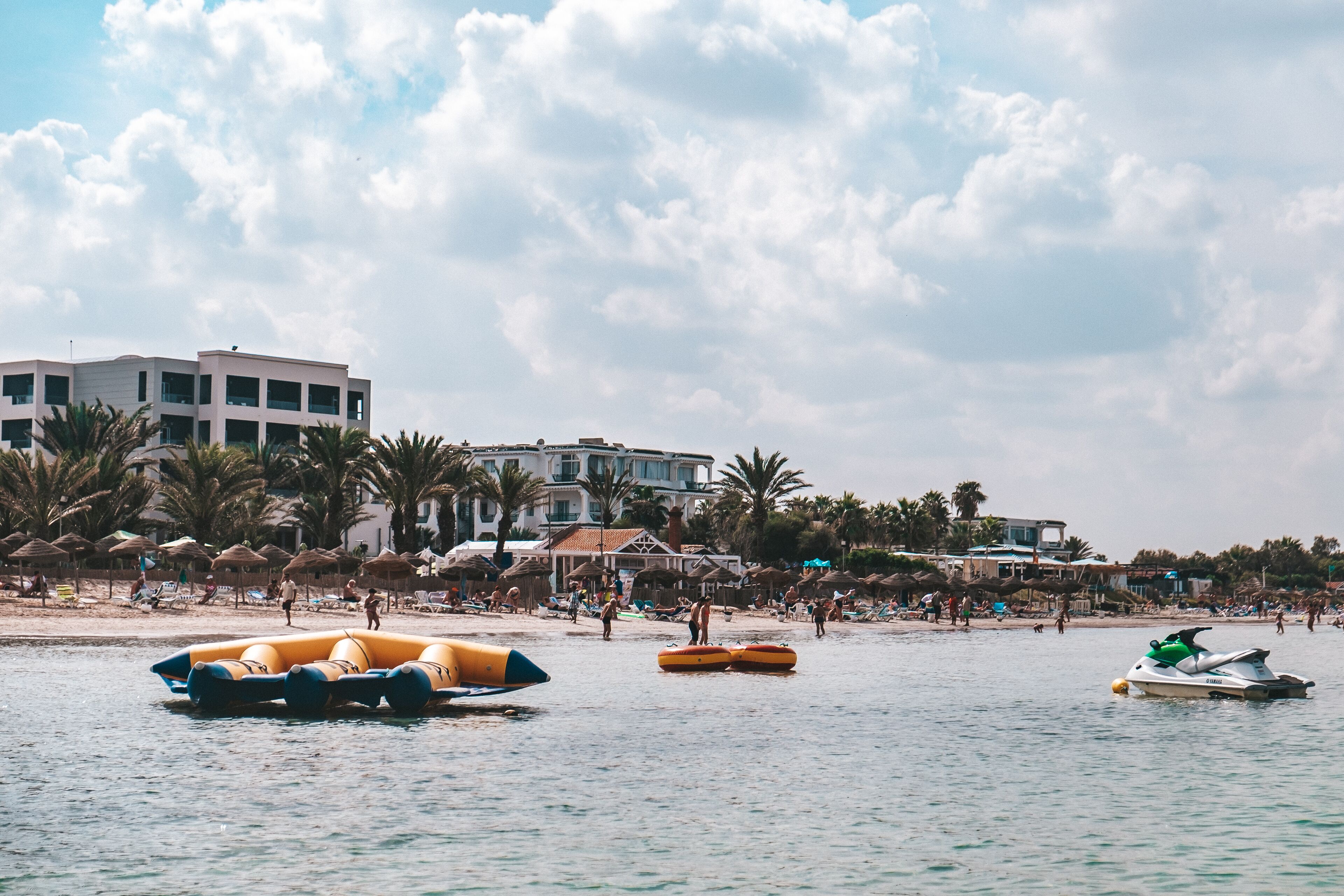 Una playa con balsas inflables, un jet ski y un edificio con varios balcones.