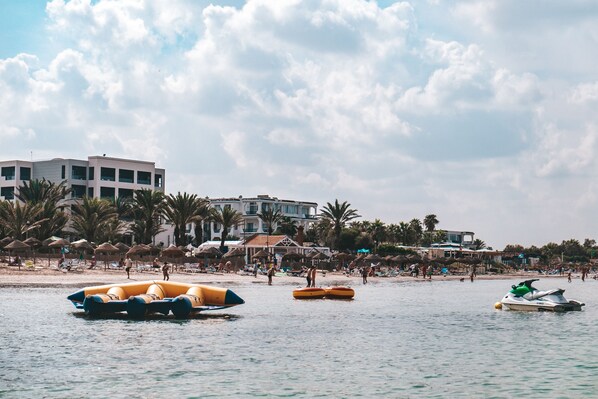 A beach with inflatable rafts, a jet ski, and a building with multiple balconies.