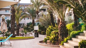 Un patio de resort con palmeras, zona de piscina y un edificio con balcones.