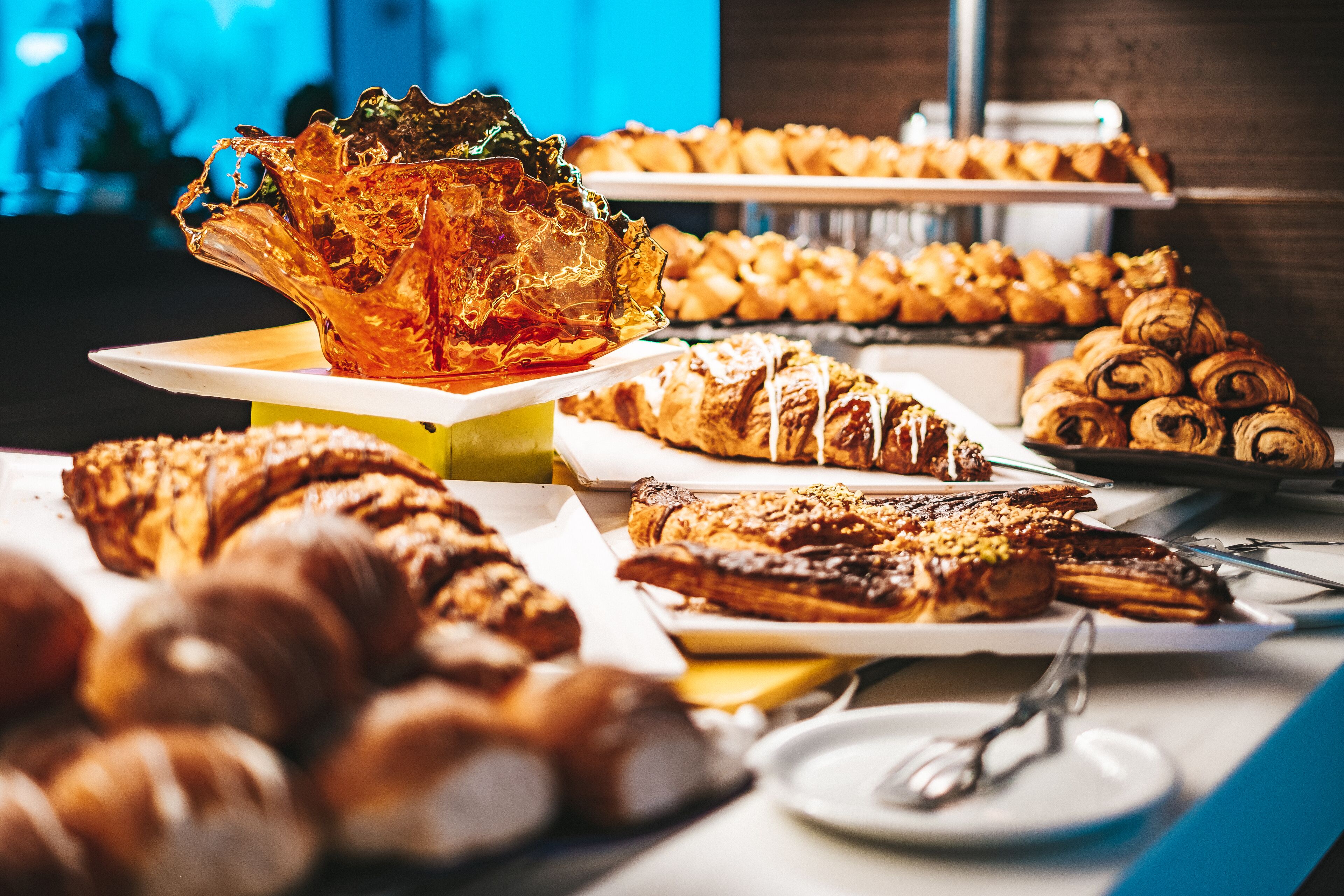 Un bufé con diversos pasteles y postres, incluyendo cruasanes y un gran cuenco de vidrio decorativo.