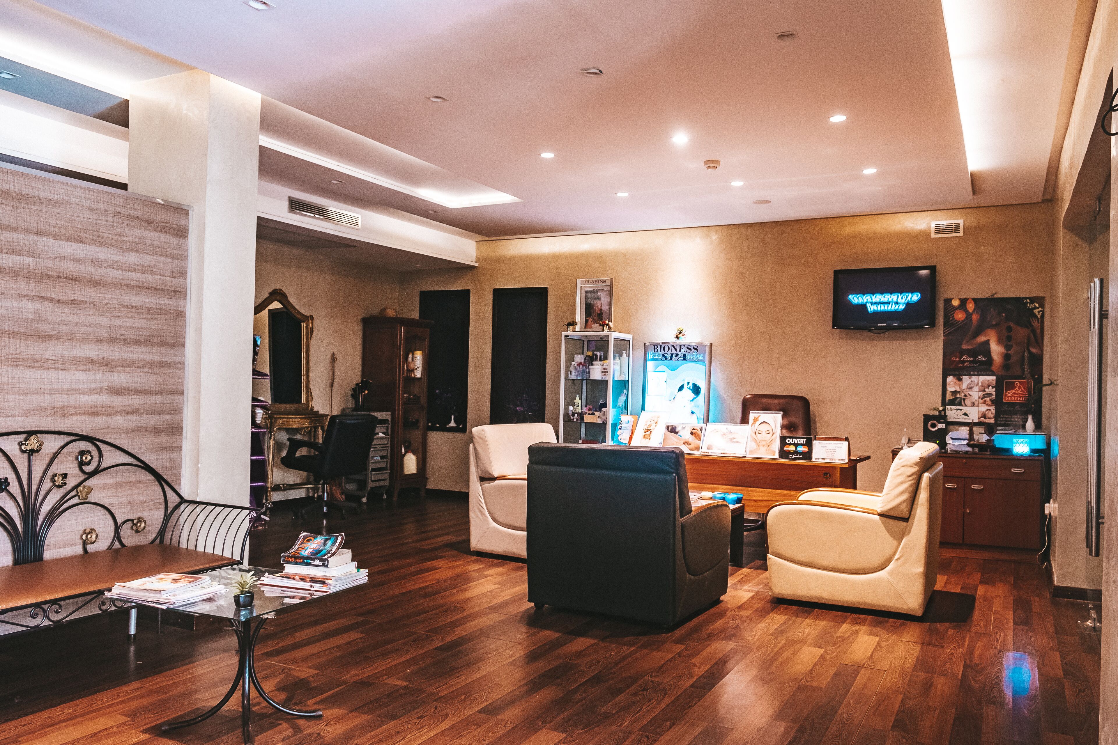Um lobby de hotel moderno com piso de madeira, balcão de recepção, cadeira de massagem, sofá e televisão fixada na parede.