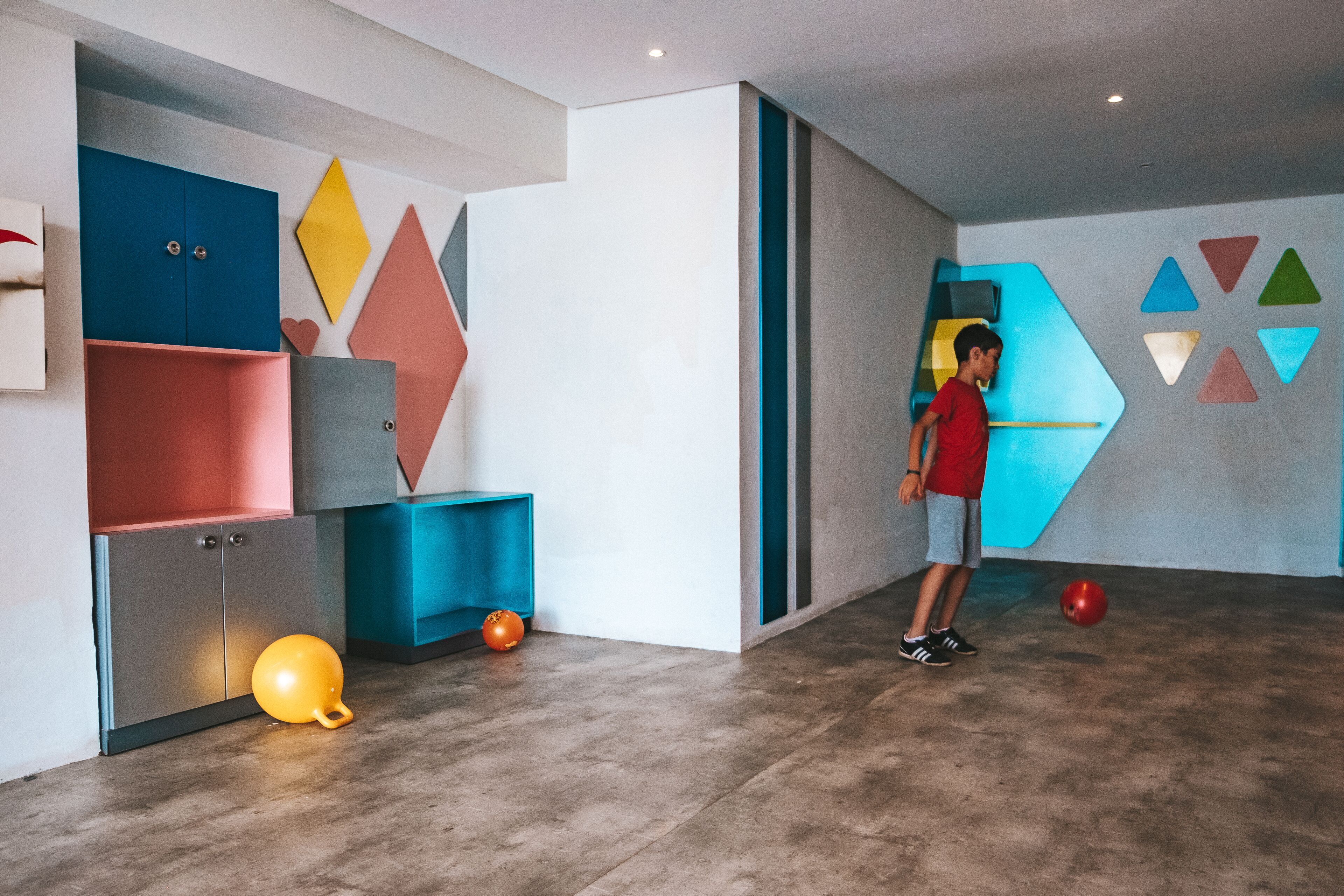 A modern interior with geometric wall designs, a child playing with balls, and a variety of storage units.