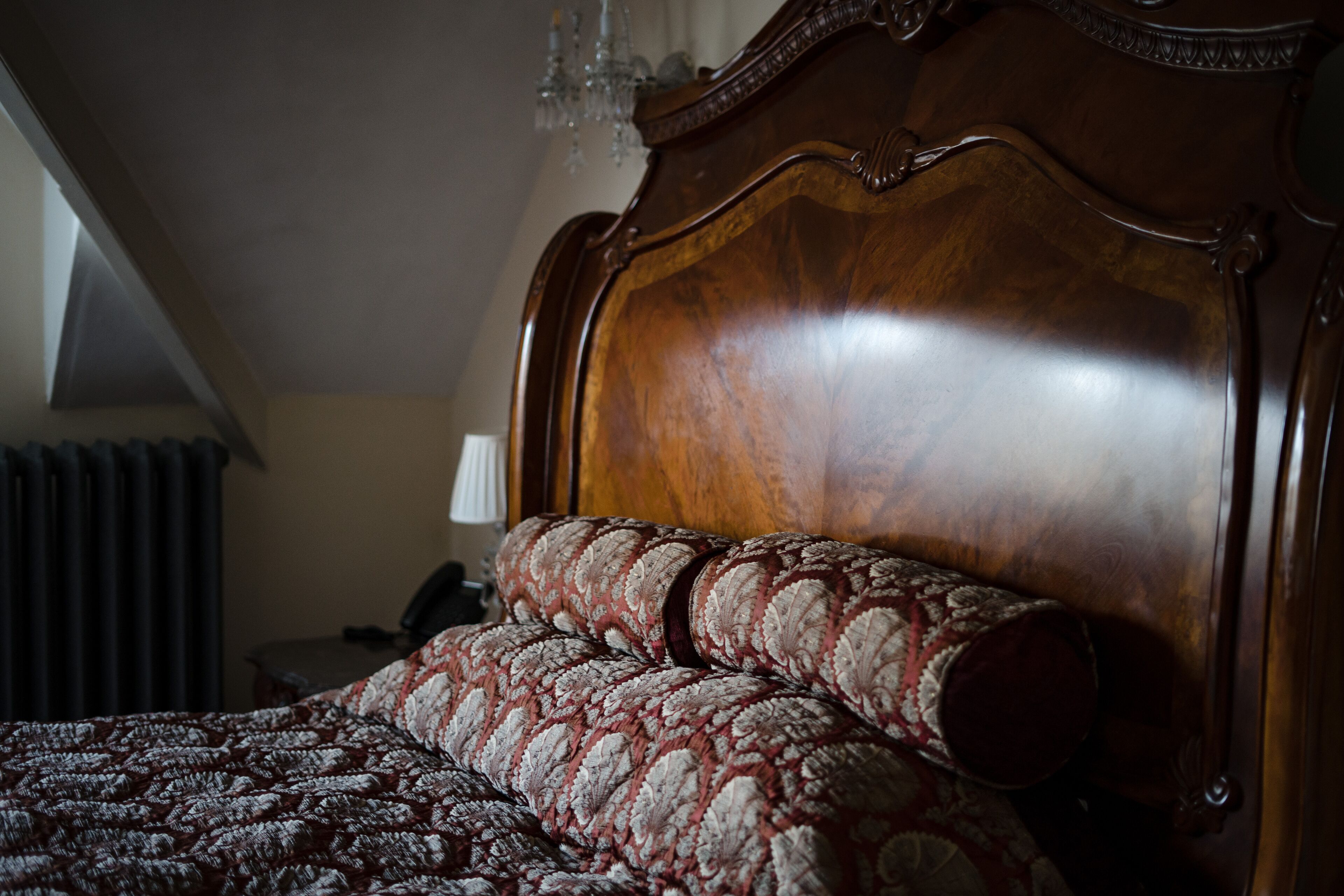 A wooden bed with a headboard, a patterned bedspread, and a lamp on a bedside table.