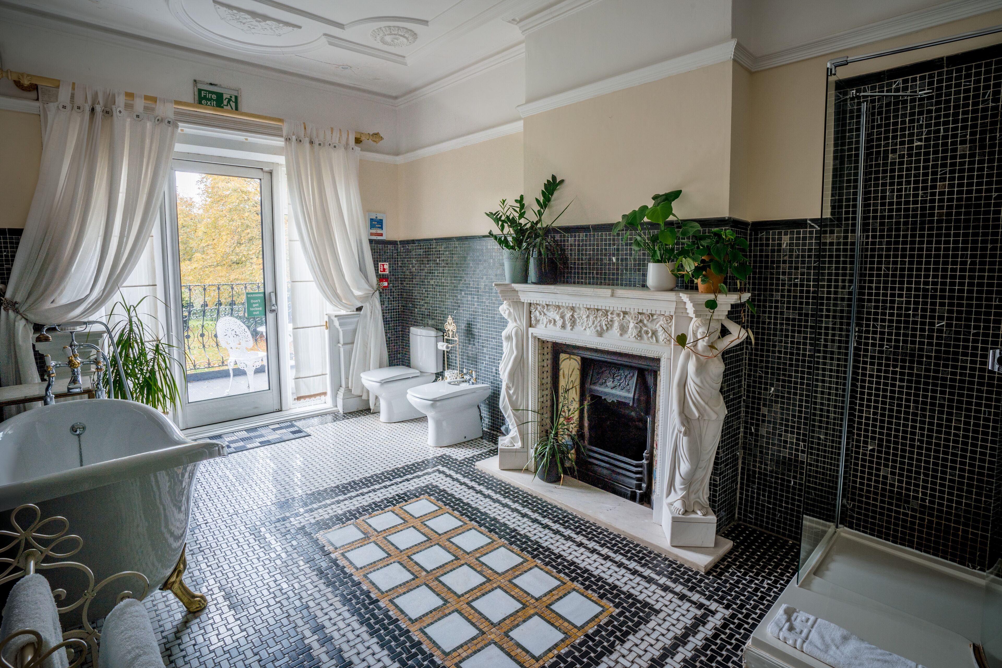 A bathroom with a freestanding bathtub, a white marble fireplace, and a tiled floor with a geometric pattern.