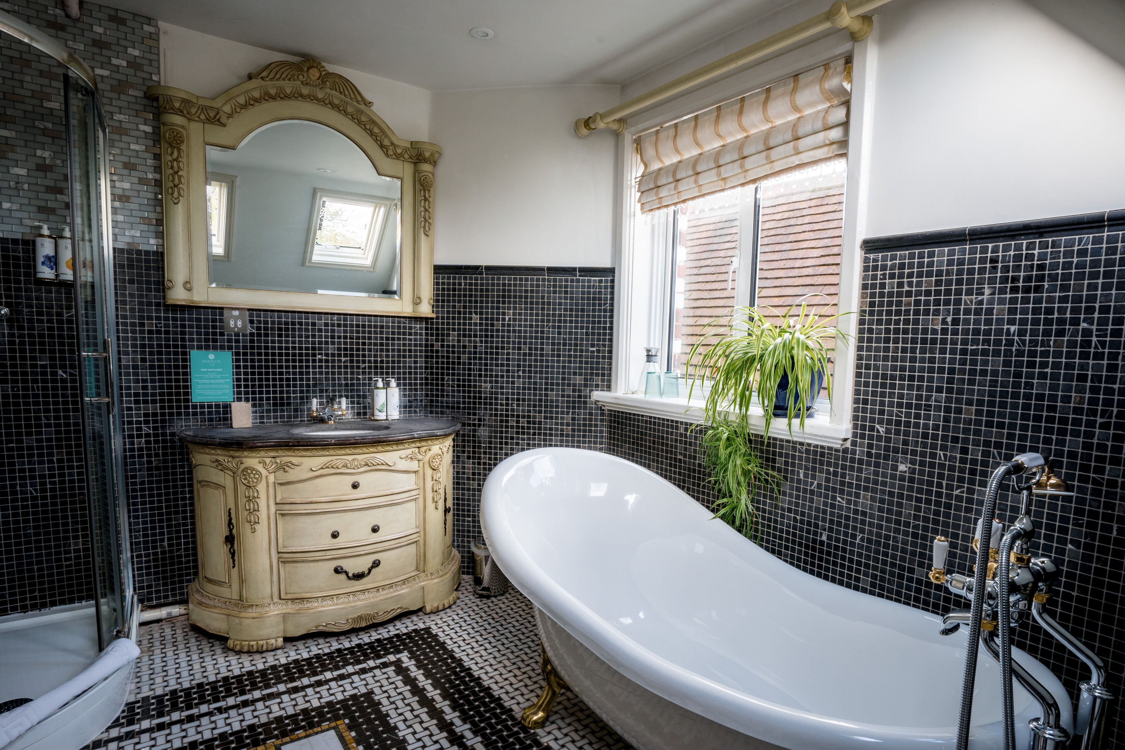 A bathroom with a freestanding bathtub, a vanity with drawers, a large mirror, and a window with blinds.