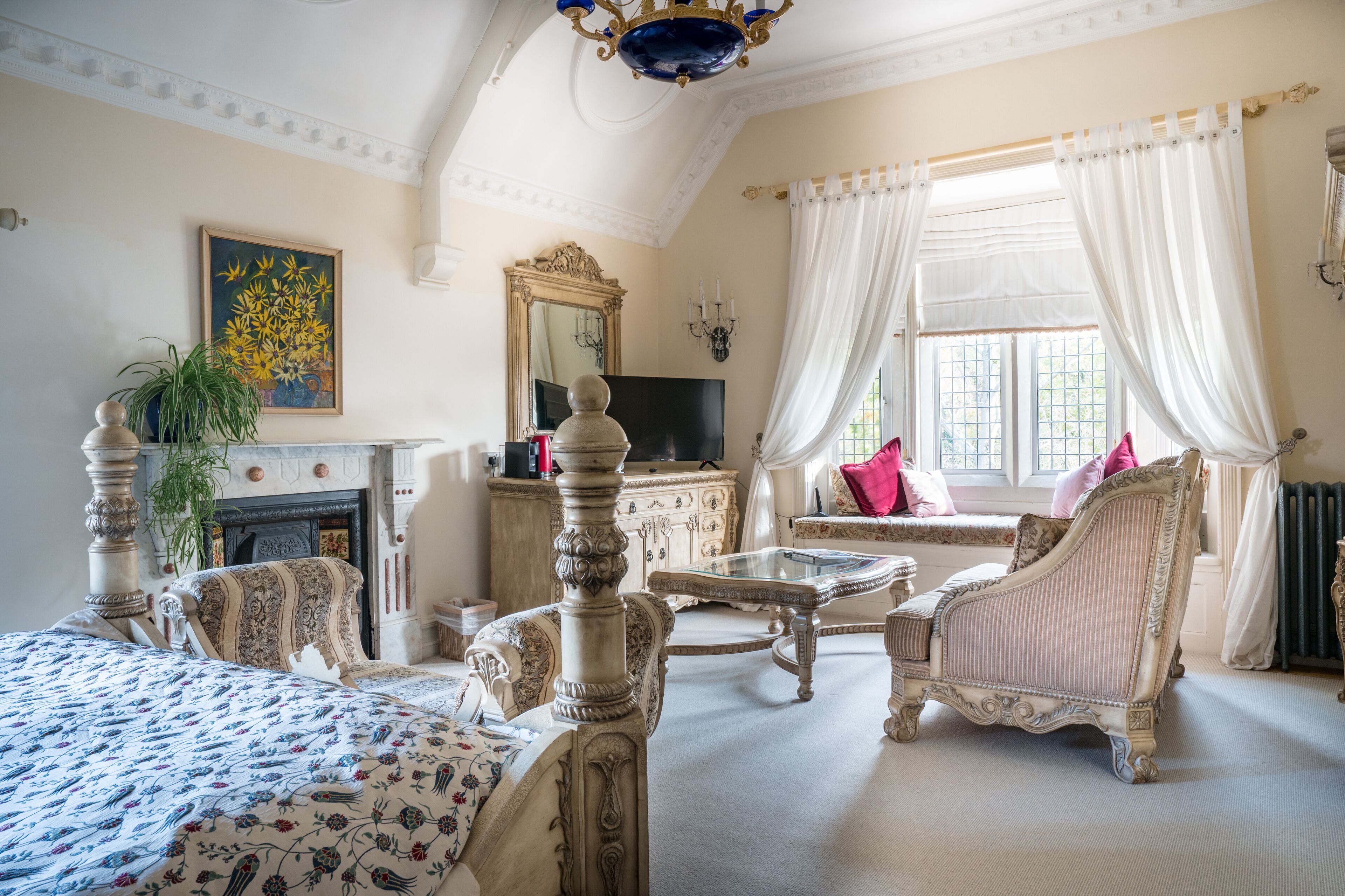 A classic room with a bed, a sofa, a television, and a fireplace.