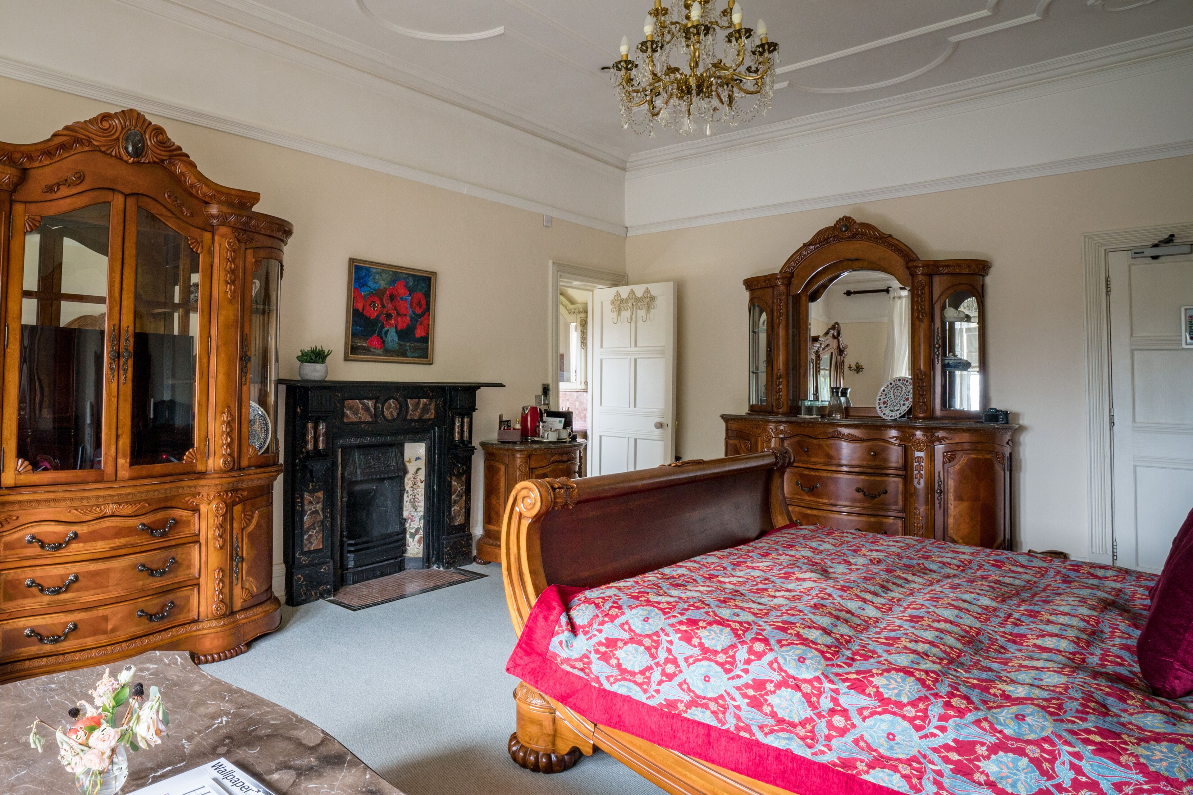 A classic bedroom with a large wooden bed, a wooden dresser, a mirror, and a fireplace.