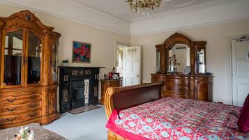 A classic bedroom with a large wooden bed, a wooden dresser, a mirror, and a fireplace.