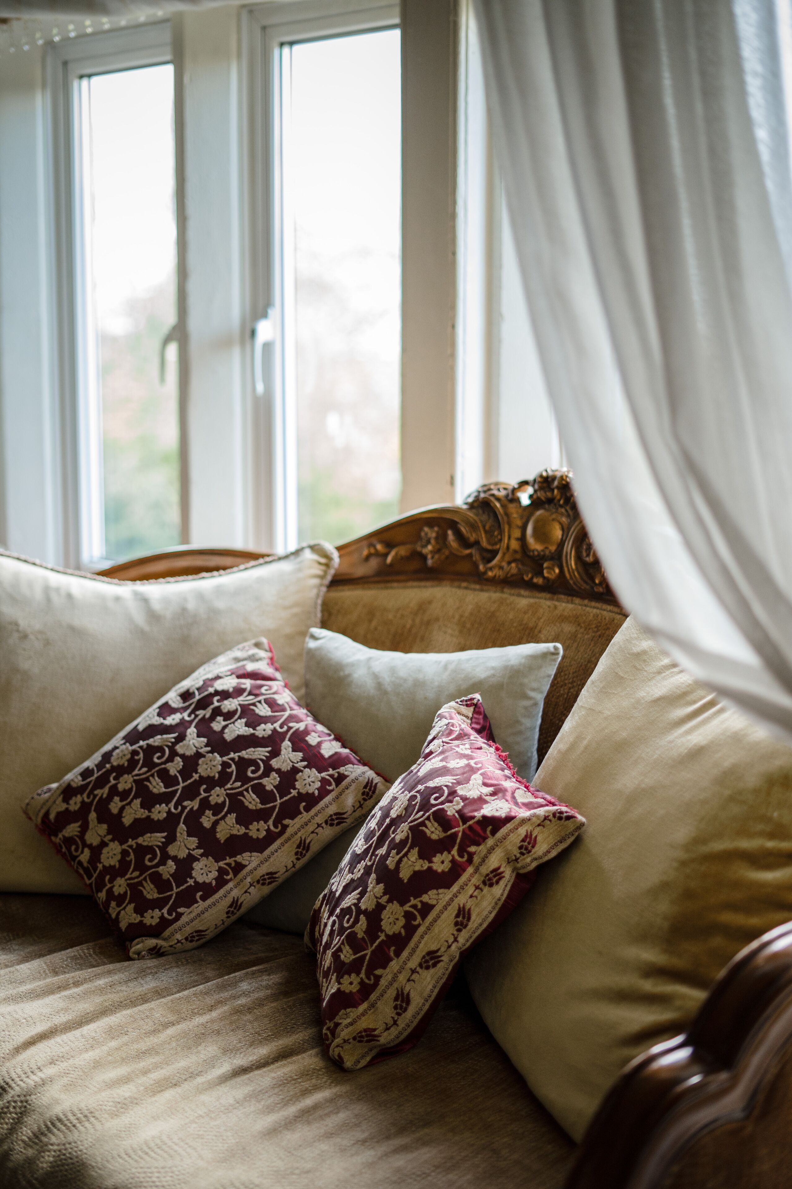 A bed with a headboard, two patterned pillows, and a window with curtains.