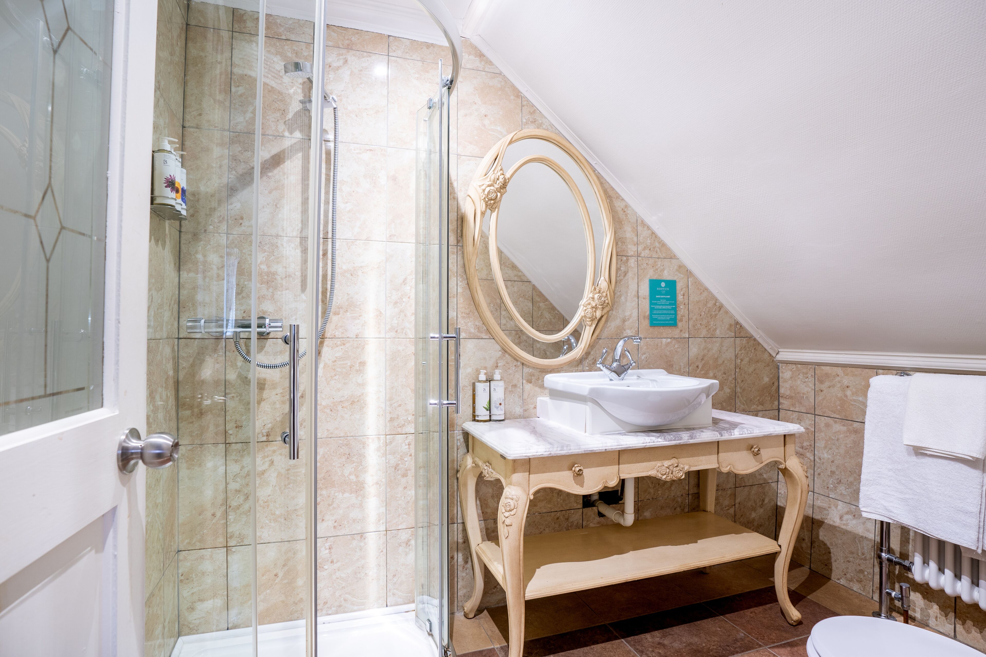 Un baño con ducha envuelta en cristal, un lavabo con encimera de mármol y un espejo grande y decorativo.