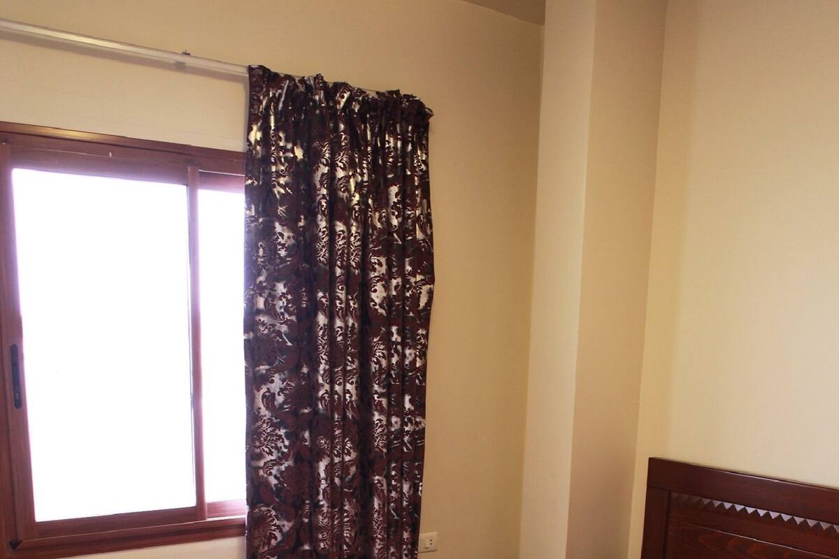 A bedroom with a wooden bed, a window with curtains, and a carpet.