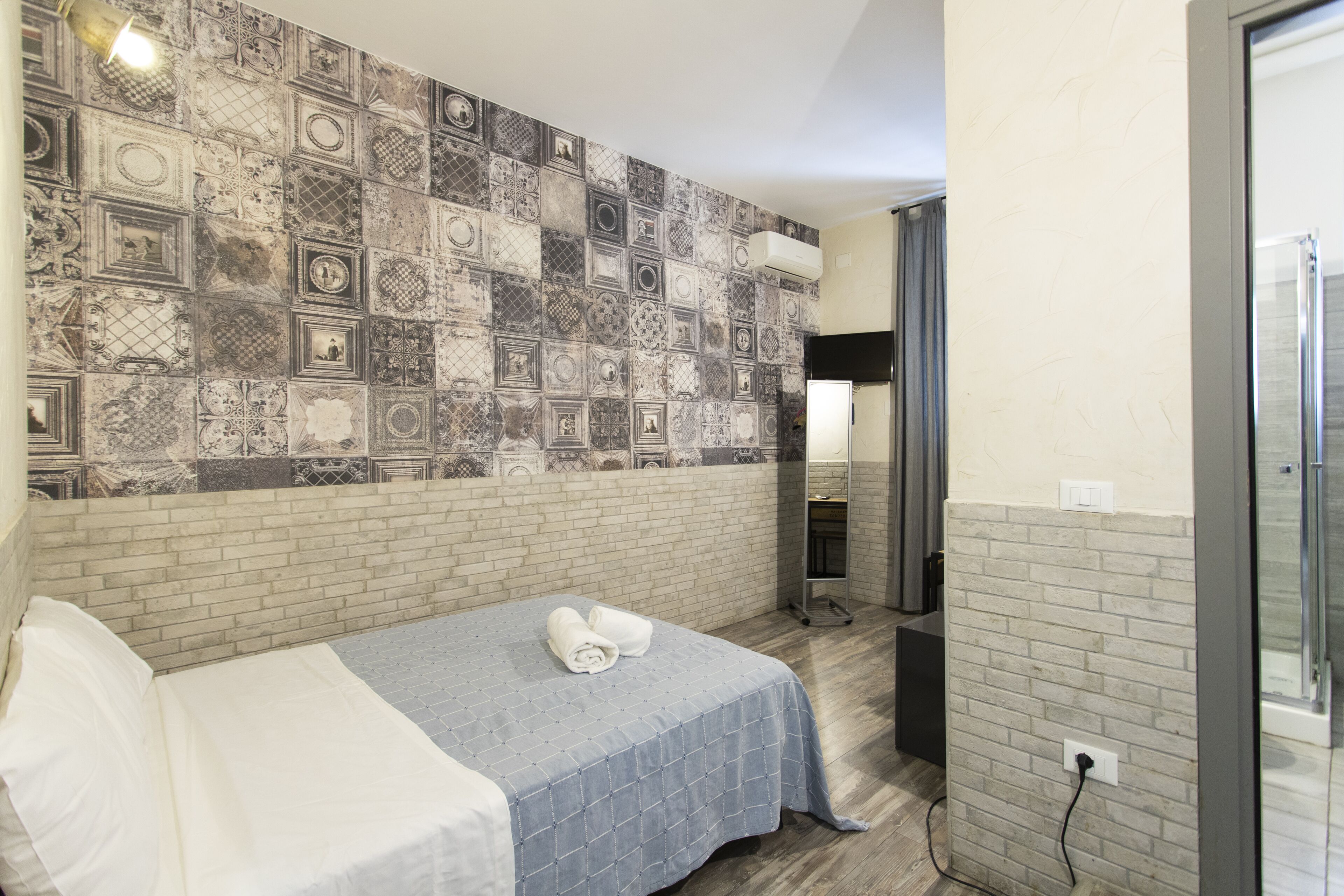 Ein Hotelzimmer mit Bett, einer Wand mit Mosaikmuster, einer Ziegelwand, einem Badezimmer mit Dusche und einem Fenster.