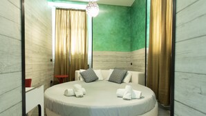 Una cama redonda con colchón y almohadas blancos, una silla roja y una mesita en una habitación con paredes de madera y una pared de acento verde.