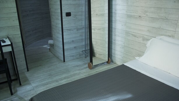 Habitación de hotel con cama, una mesita y zona de ducha.