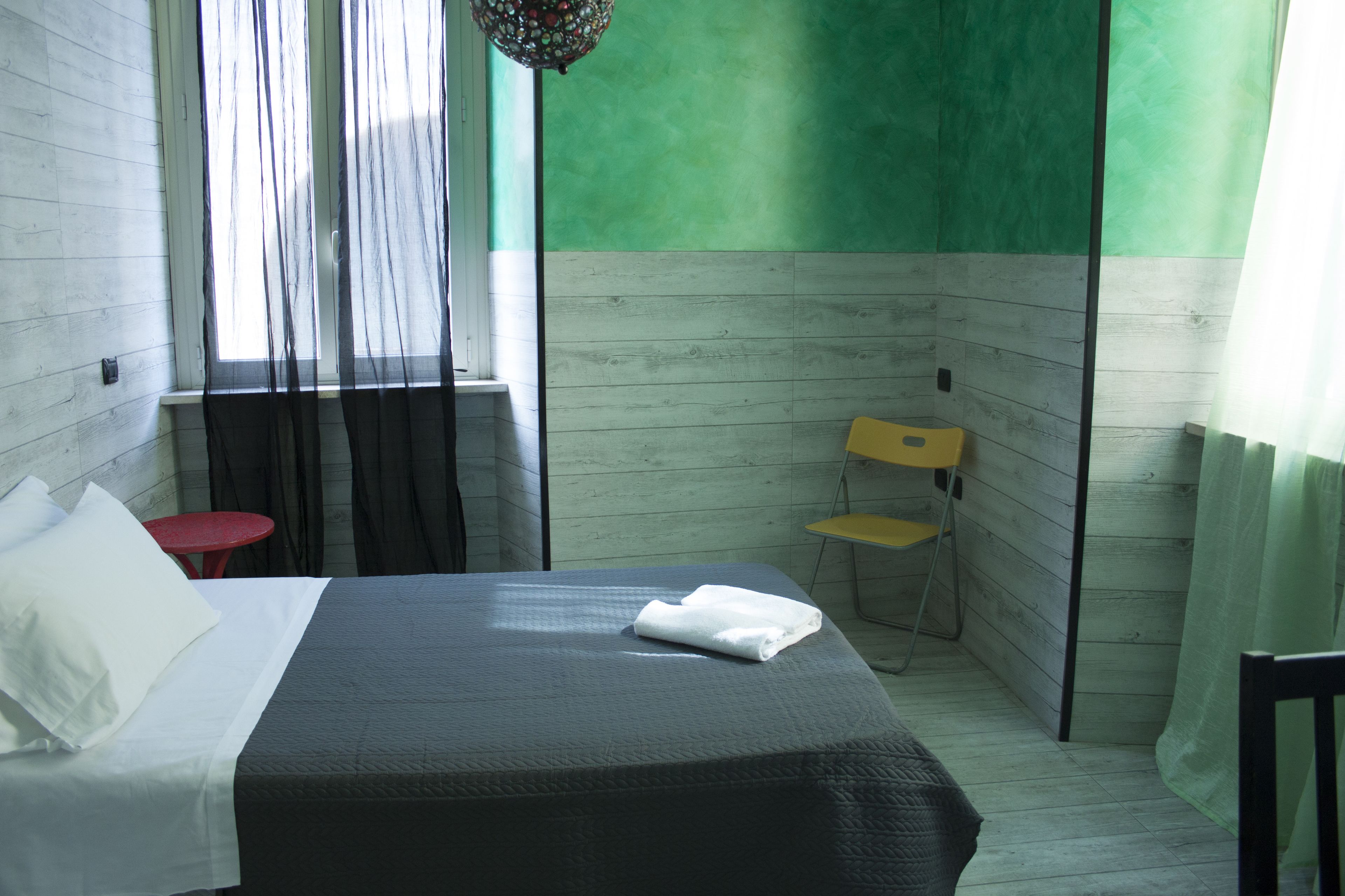 A hotel room with a bed, a small table, a chair, and a window with curtains.
