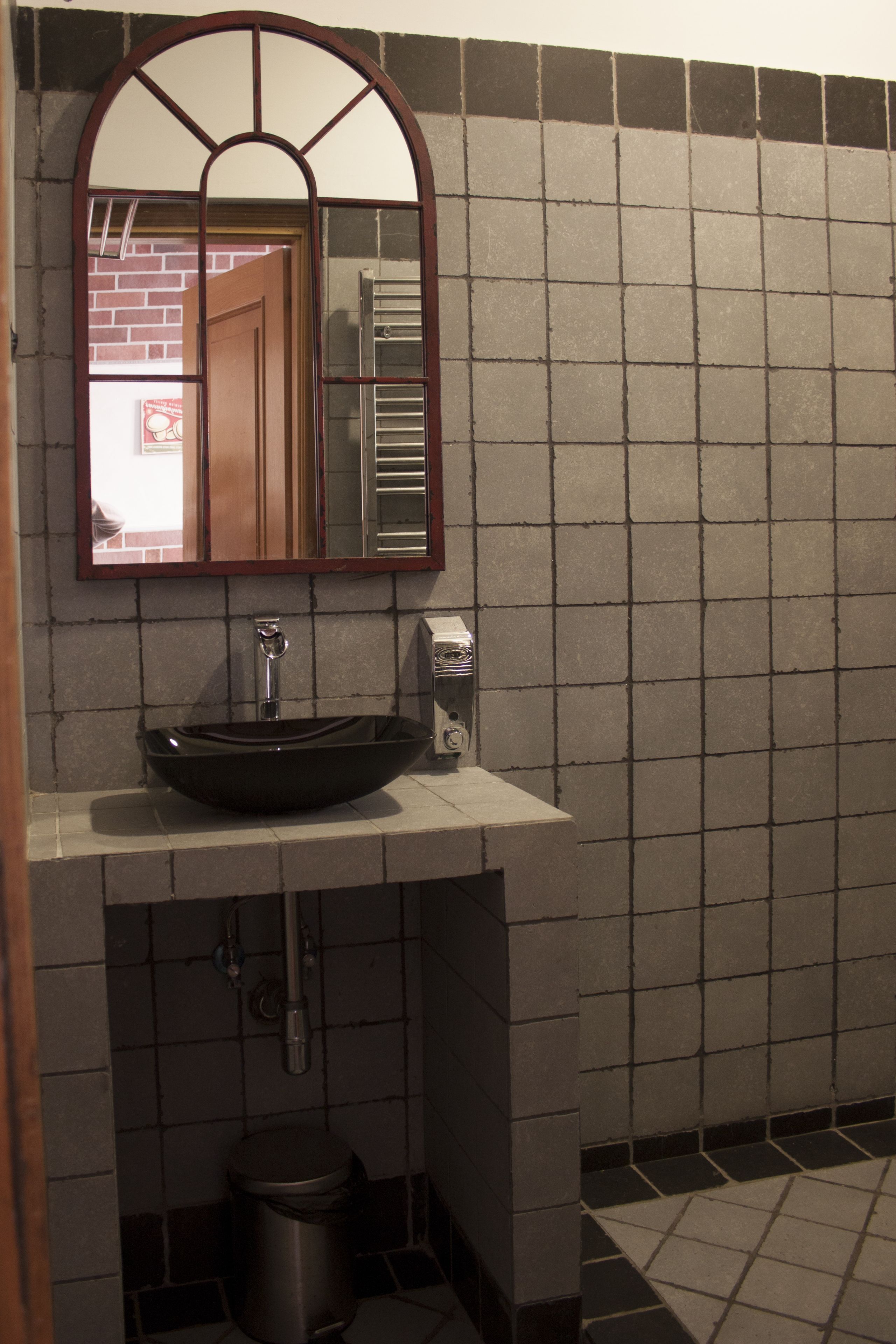 A bathroom with a black vessel sink, a mirror with a wooden frame, and tiled walls.