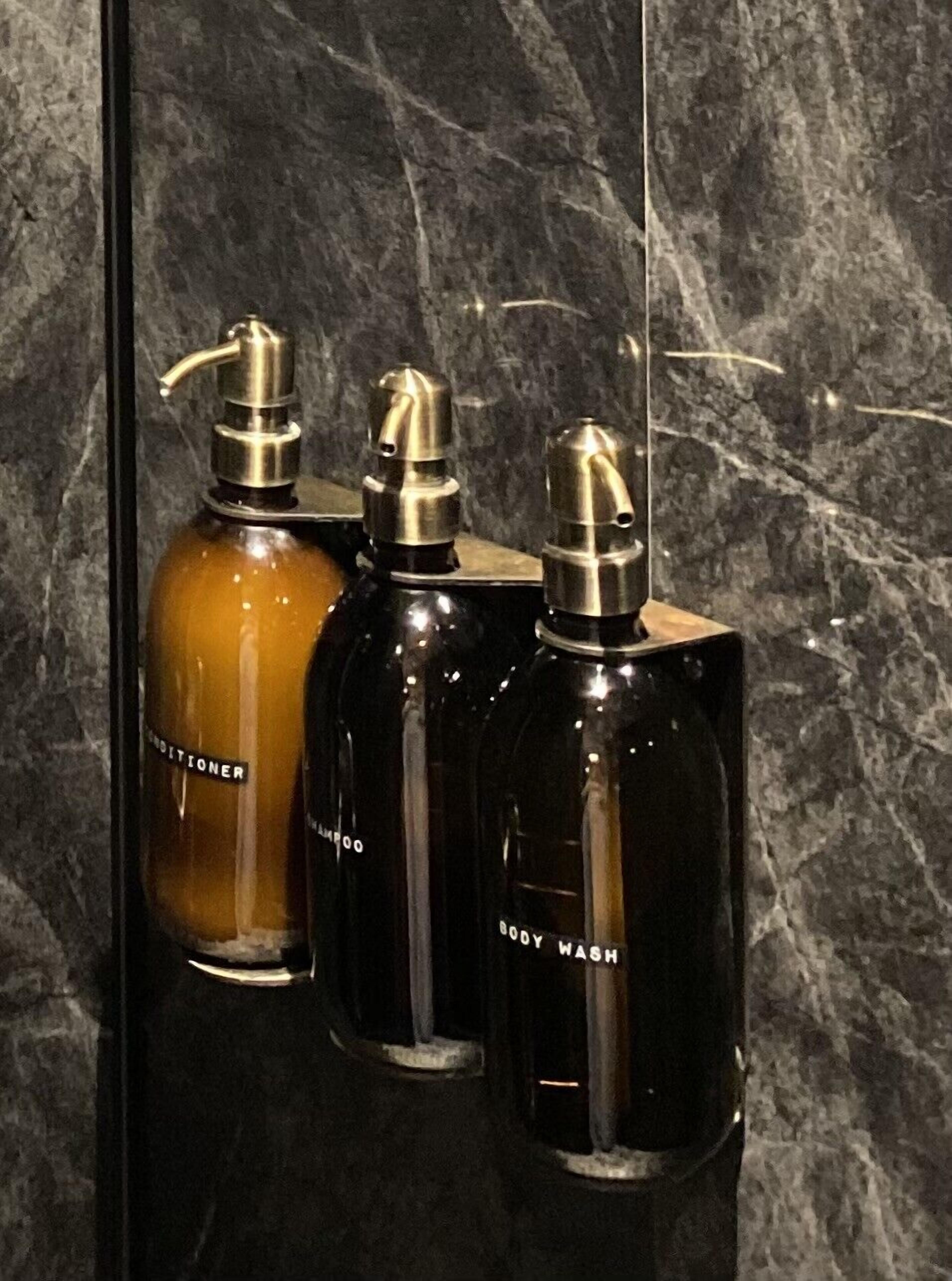 Drei Flaschen Duschgel und Conditioner in einem Badezimmer mit Marmorwand.