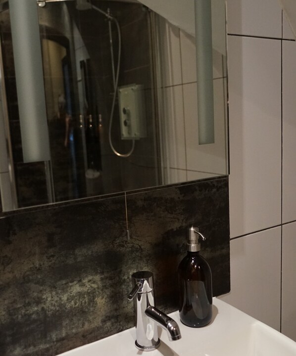 A bathroom with a modern sink, a mirror, and a shower visible in the reflection. - The Poplars Boutique (Lincoln)