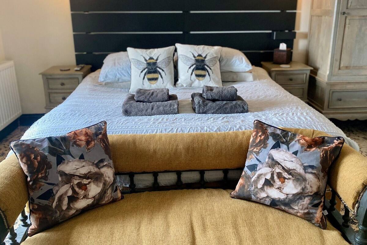 A neatly made bed with a headboard, two pillows with a bee design, and a floral throw pillow.