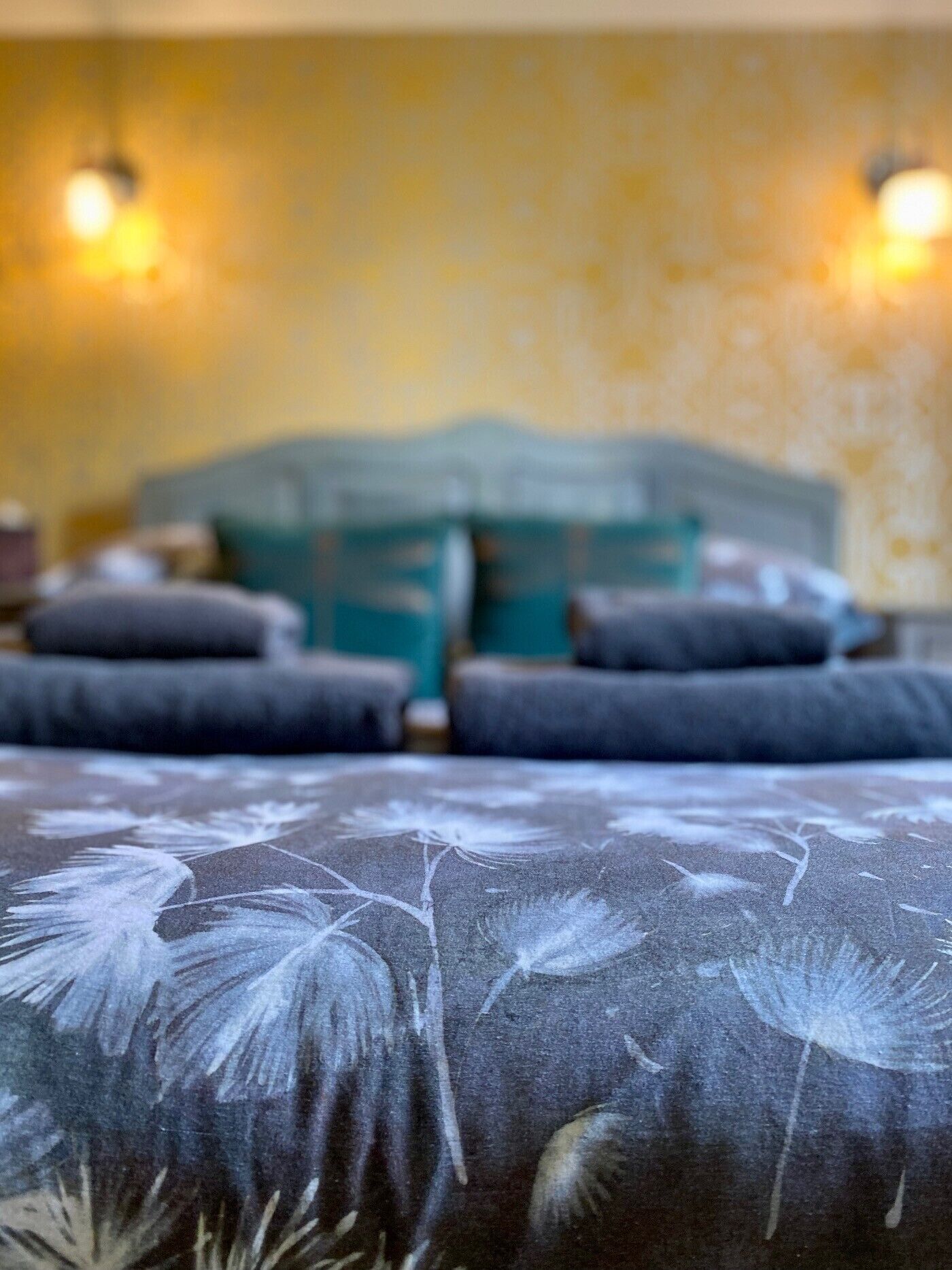 Una cama con estampado floral, cabecera y dos lámparas fijadas a la pared.