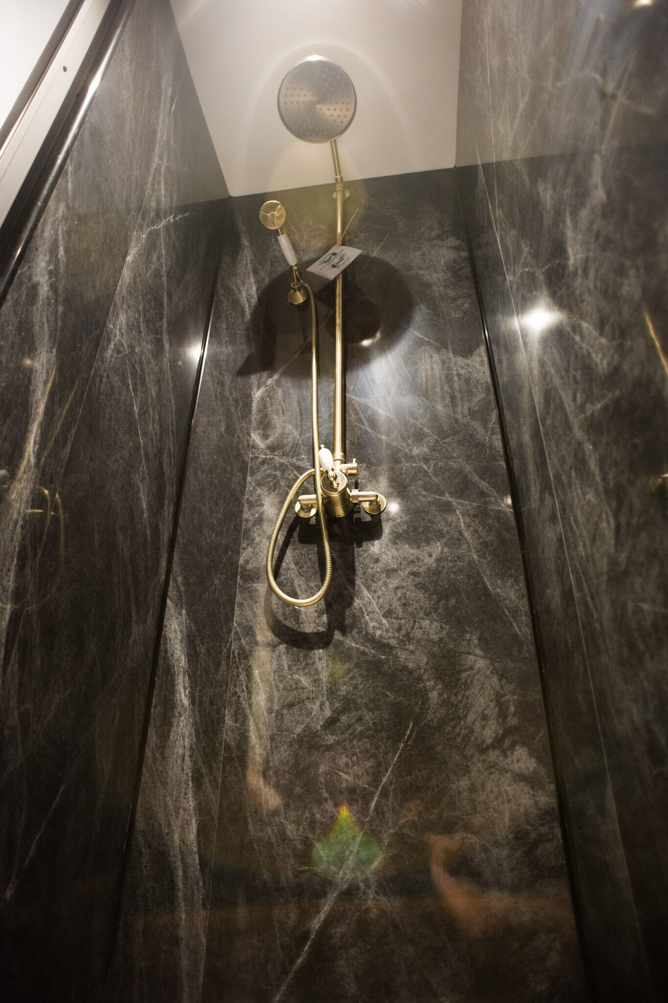 Een douche met een handdouche en een handspiegel aan de wand bevestigd.