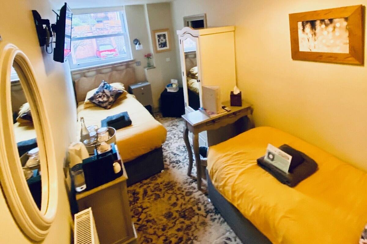 A compact hotel room with a bed, a desk, a chair, a mirror, and a window.