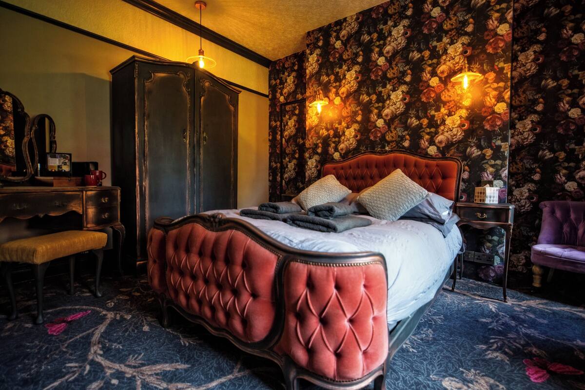 A bedroom with a large bed, a wardrobe, a vanity with a mirror, and a chair.