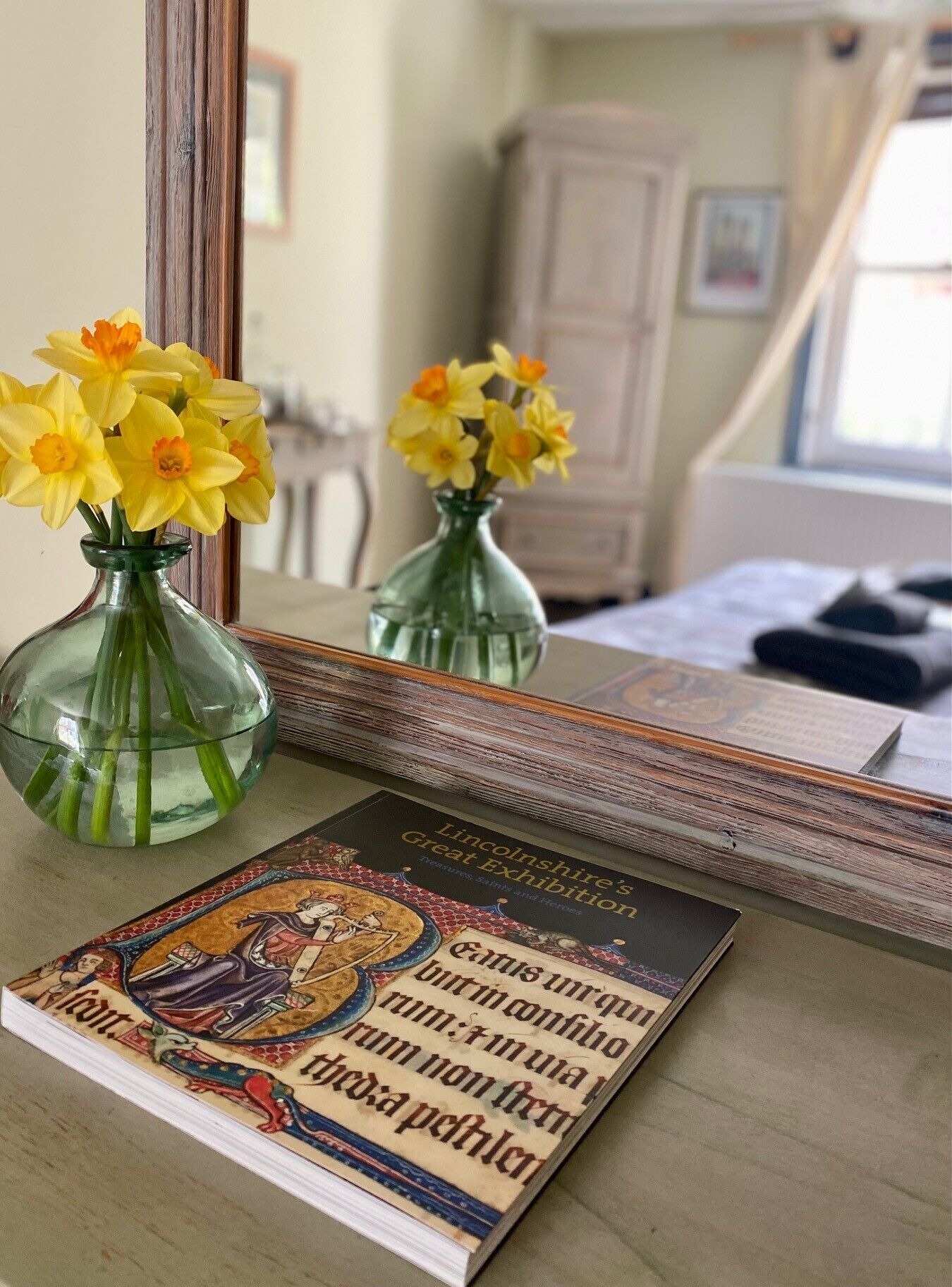 En bog med titlen "Lincolnshire's Great Exhibition" på et bord med to vaser fyldt med påskeliljer.